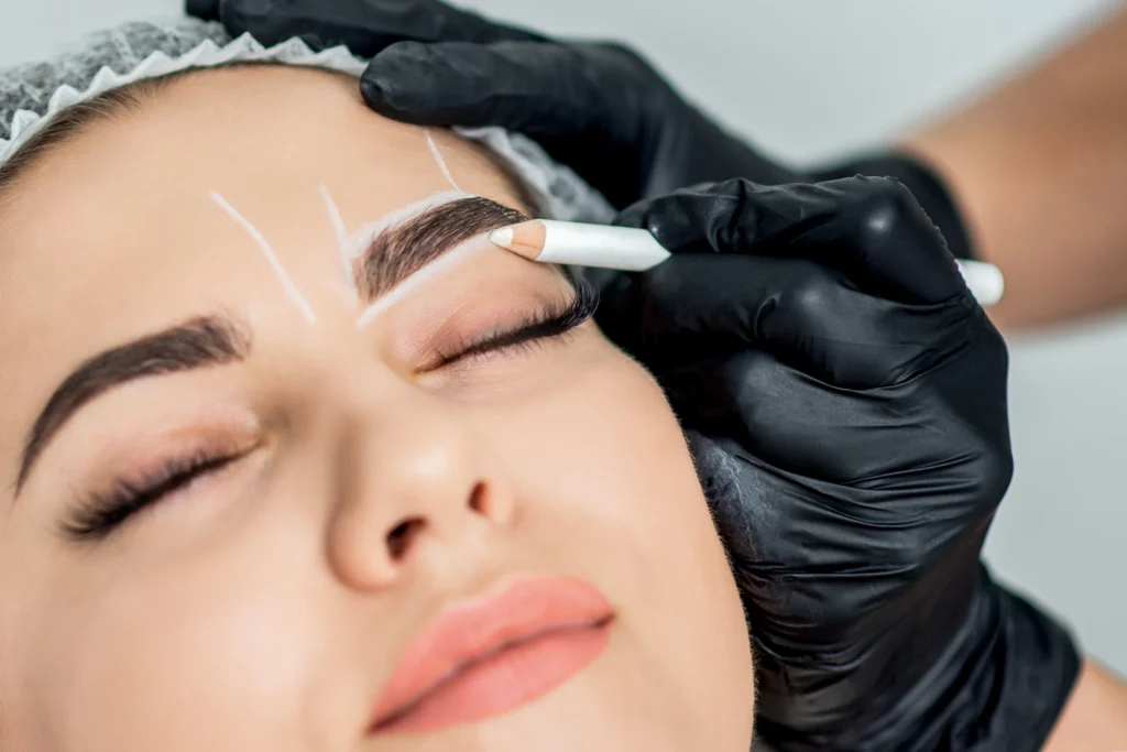 Profesional marcando la guía para diseño de cejas perfectas con lápiz blanco sobre cejas de cliente.