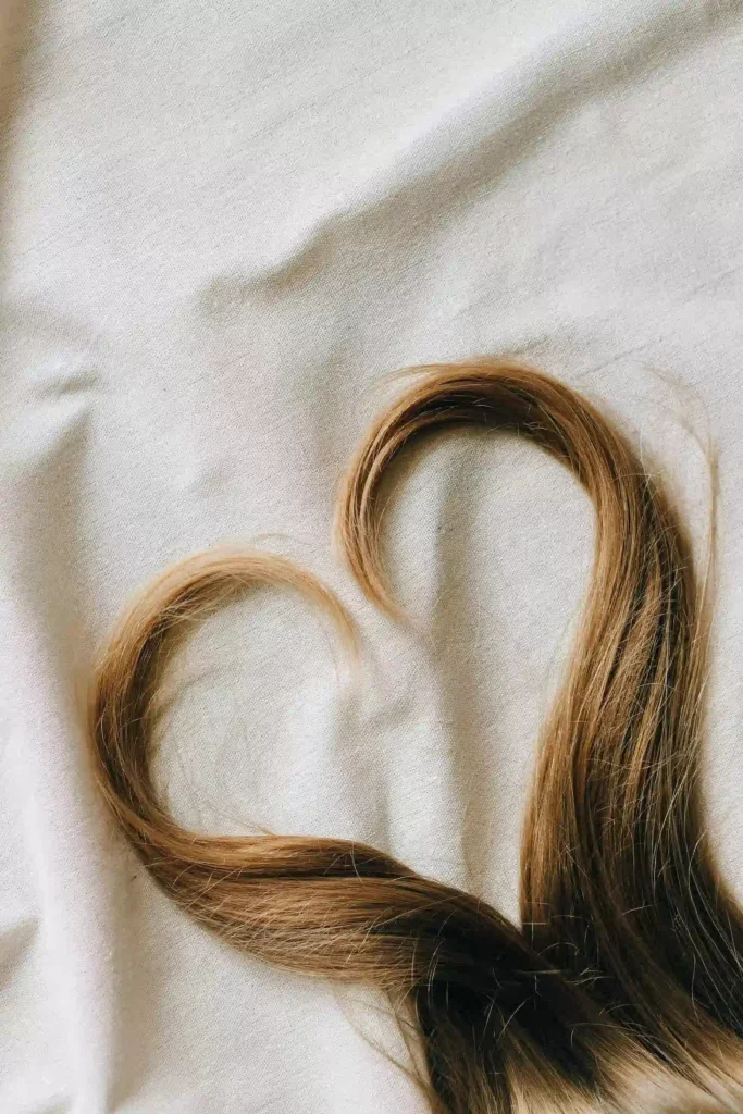 Mechones de cabello castaño y rubio dispuestos en forma de corazón sobre una tela clara