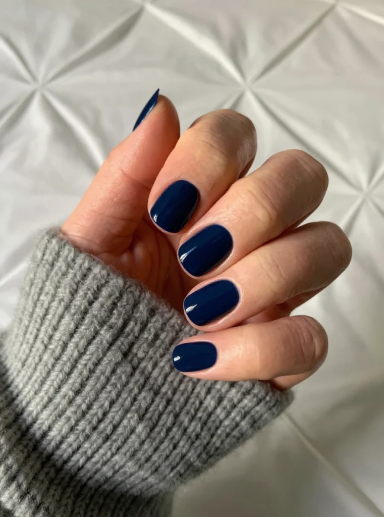 Uñas cortas almendradas en azul marino con jersey gris.