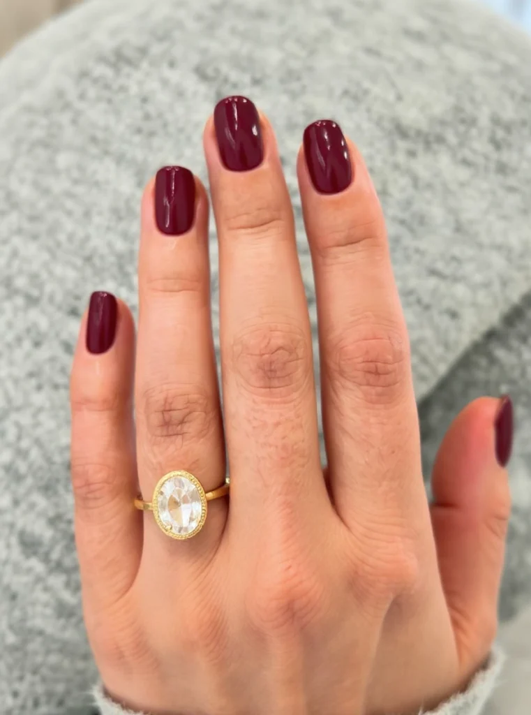 Uñas almendradas color granate con diseño minimalista y detalles dorados elegantes.