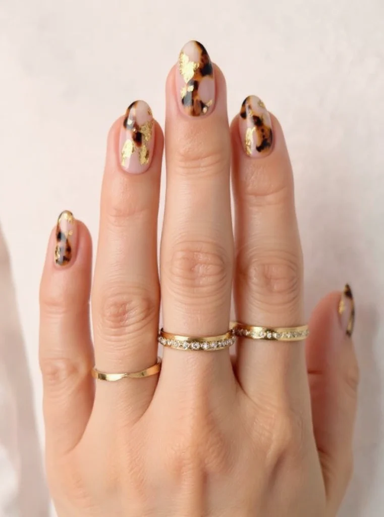 Uñas largas almendradas con láminas doradas sobre base nude.