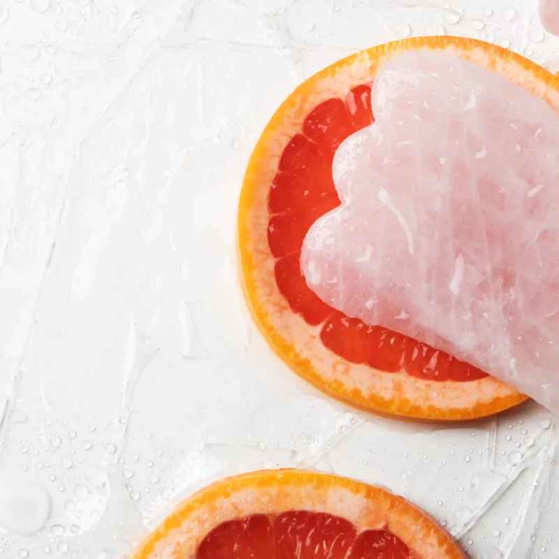 Piedra guasha acompañada de toronja, reflejando un masaje facial natural para iluminar y tonificar la piel.