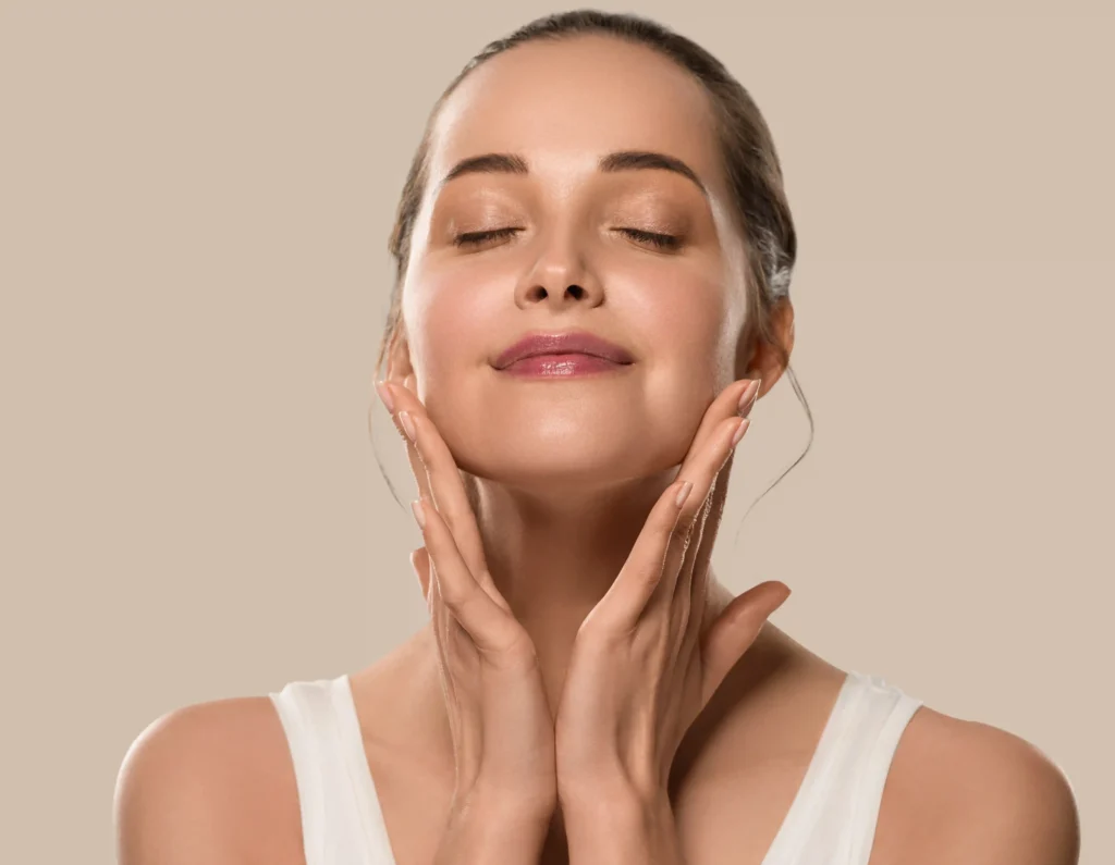 Mujer con piel radiante tocando su rostro tras una rutina de masaje facial con guasha o rodillo de jade.