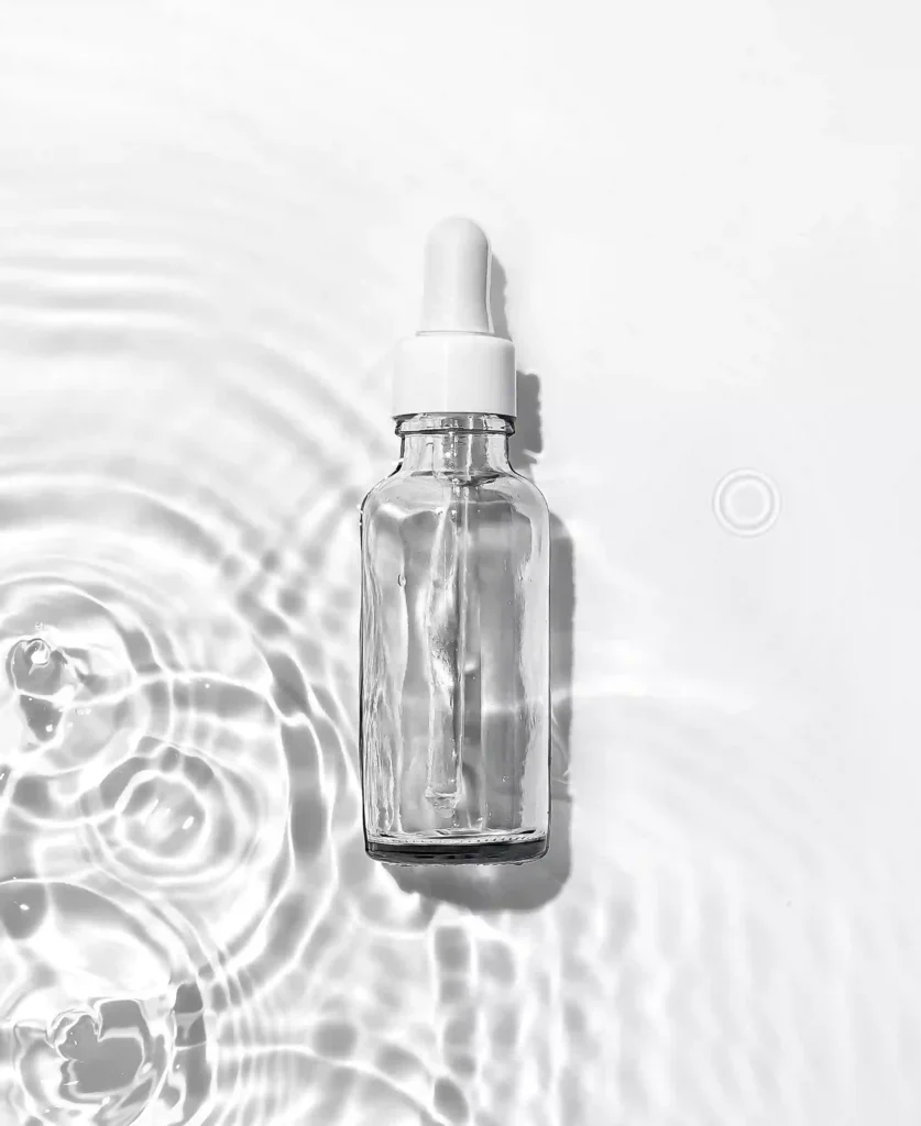 Botella de sérum sobre agua representando ingredientes hidratantes como el ácido hialurónico.