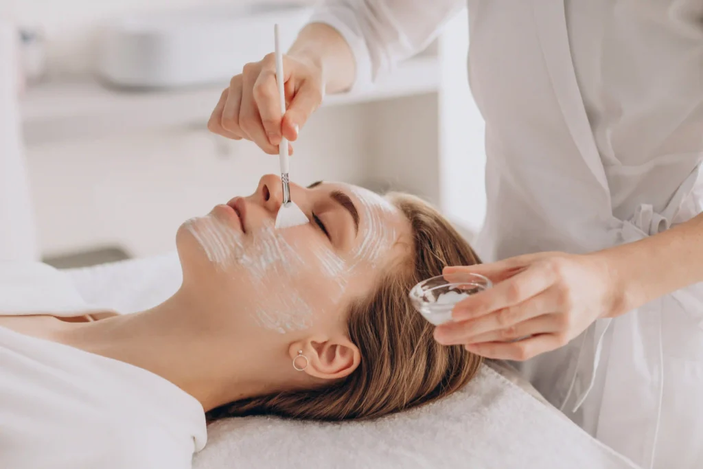 Cosmetóloga aplicando una mascarilla hidratante durante un tratamiento facial profesional.