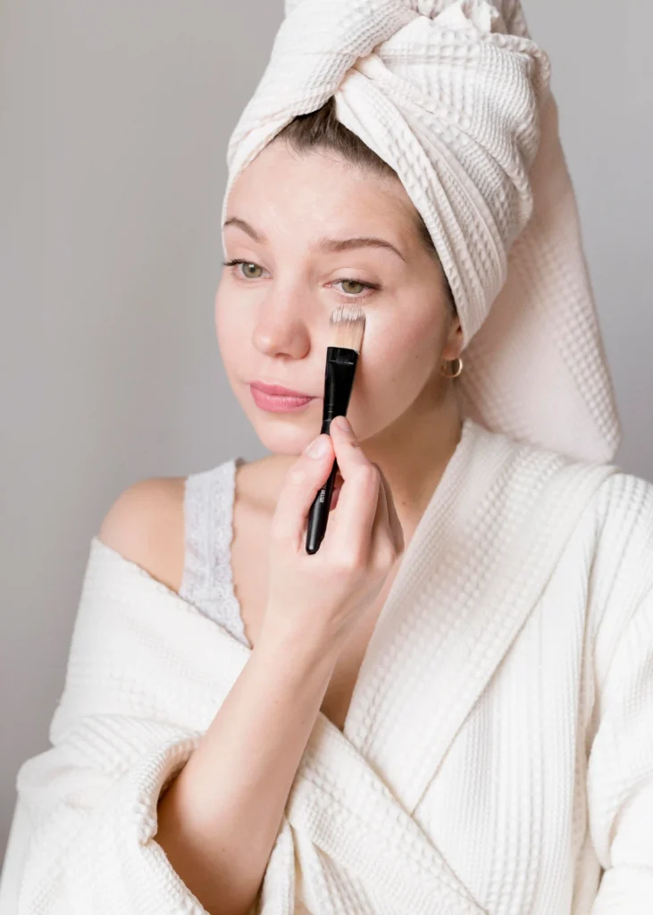 Joven mujer aplicando corrector de ojeras debajo de sus ojos