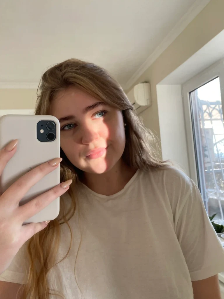 Persona observándose en el espejo mientras sostiene un teléfono, mostrando contraste entre apariencia real y filtrada