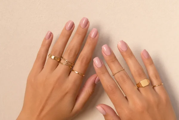 Manos con manicura rosa y varios anillos dorados de estilo minimalista