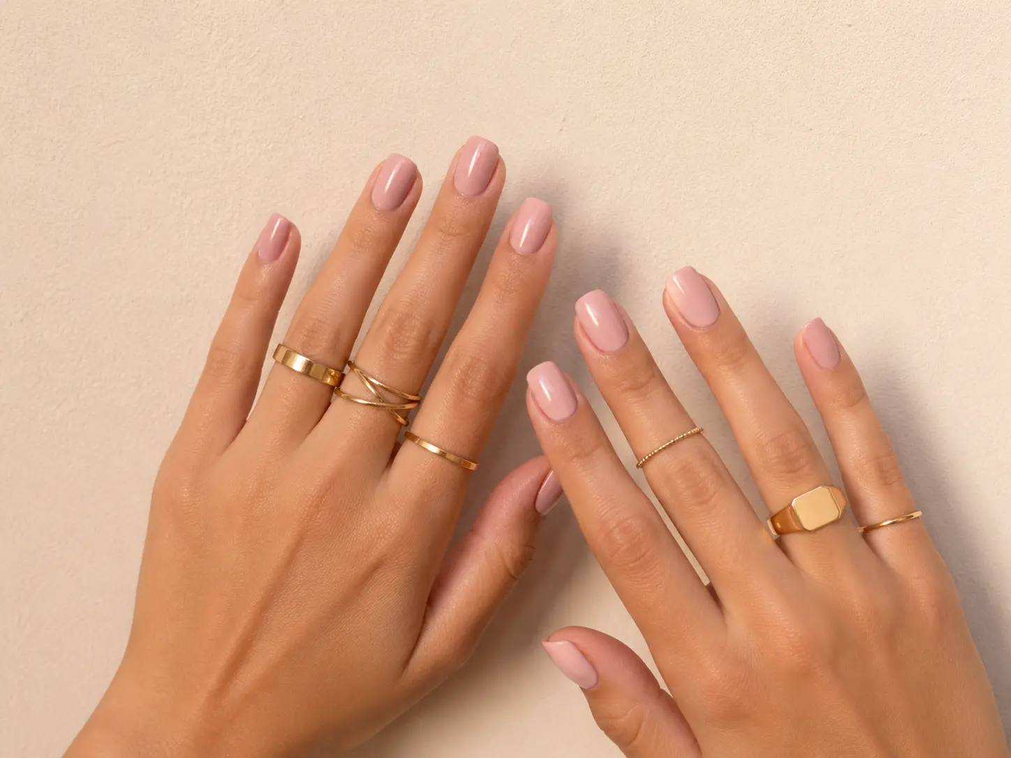 Manos con manicura rosa y varios anillos dorados de estilo minimalista