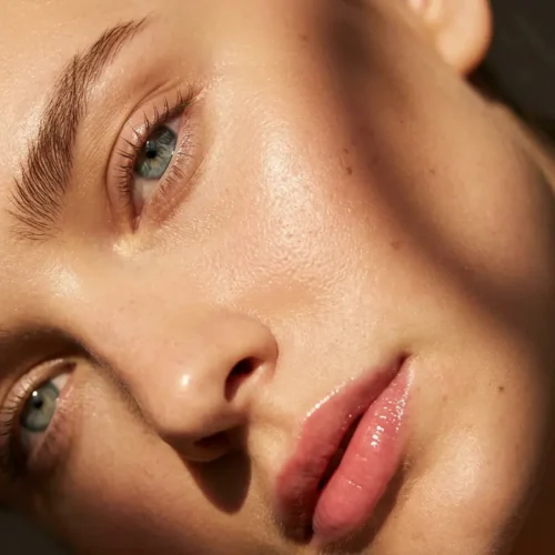 Primer plano editorial de rostro femenino con labios brillantes, piel luminosa y sombras cálidas