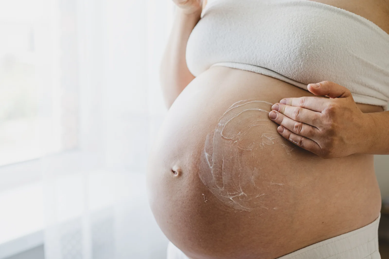 Embarazada aplicando crema en el abdomen con movimientos suaves y ascendentes.