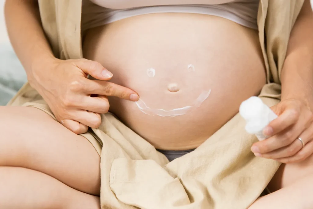 Embarazada dibujando una sonrisa con crema sobre el vientre durante su rutina de cuidado.