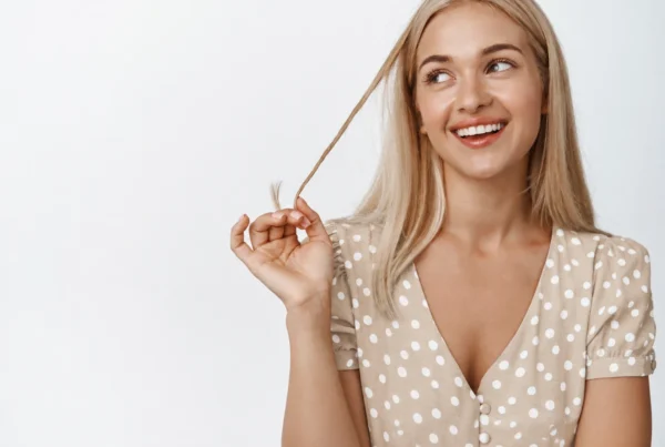 Mujer rubia sonriendo y sujetando un mechón de pelo para ilustrar el crecimiento pelo
