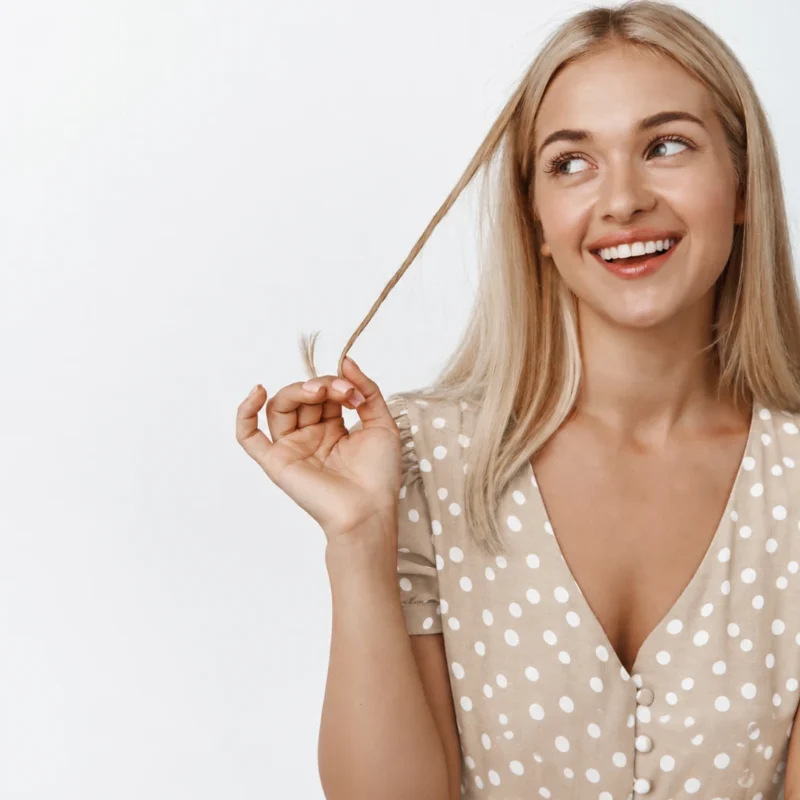 Mujer rubia sonriendo y sujetando un mechón de pelo para ilustrar el crecimiento pelo