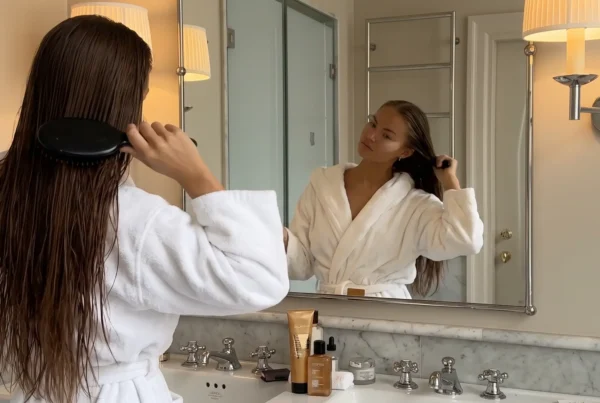 Mujer cepillando su melena húmeda frente al espejo del baño después de lavarse el pelo graso
