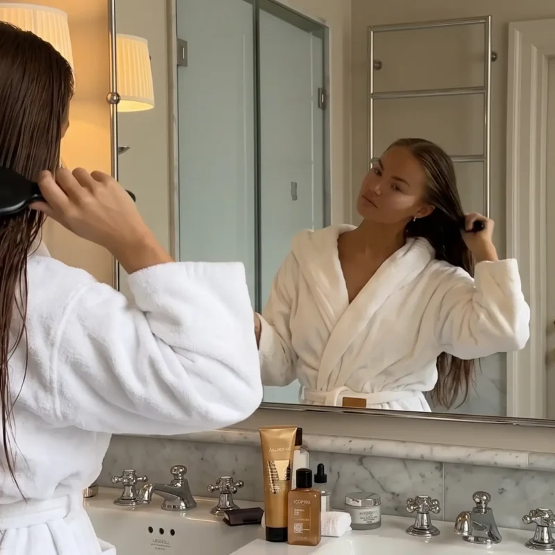 Mujer cepillando su melena húmeda frente al espejo del baño después de lavarse el pelo graso