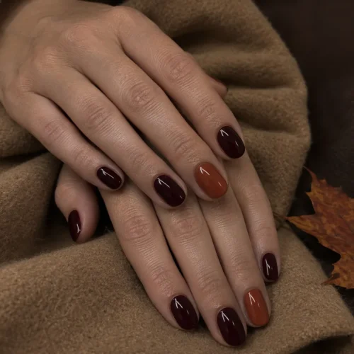 Manicura de otoño 2026 en burdeos con uña de acento terracota sobre abrigo camel