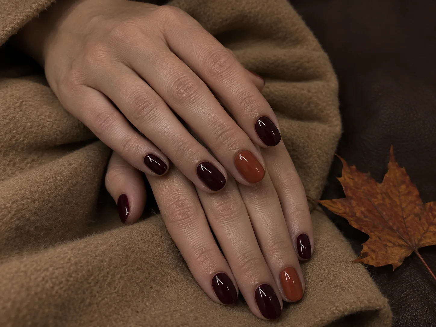 Manicura de otoño 2026 en burdeos con uña de acento terracota sobre abrigo camel